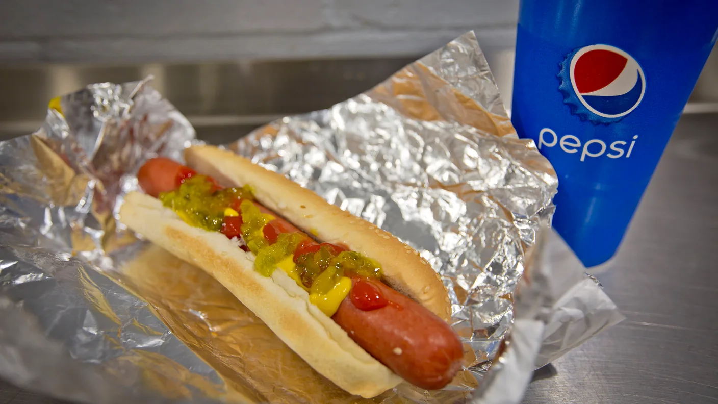 A Costco food court hot dog in foil beside a Pepsi cup